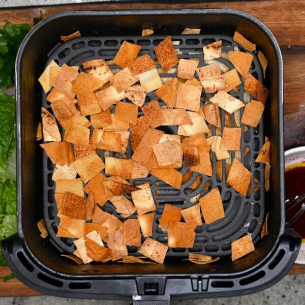Pita chips in an air fryer basket, toasted for fattoush salad.