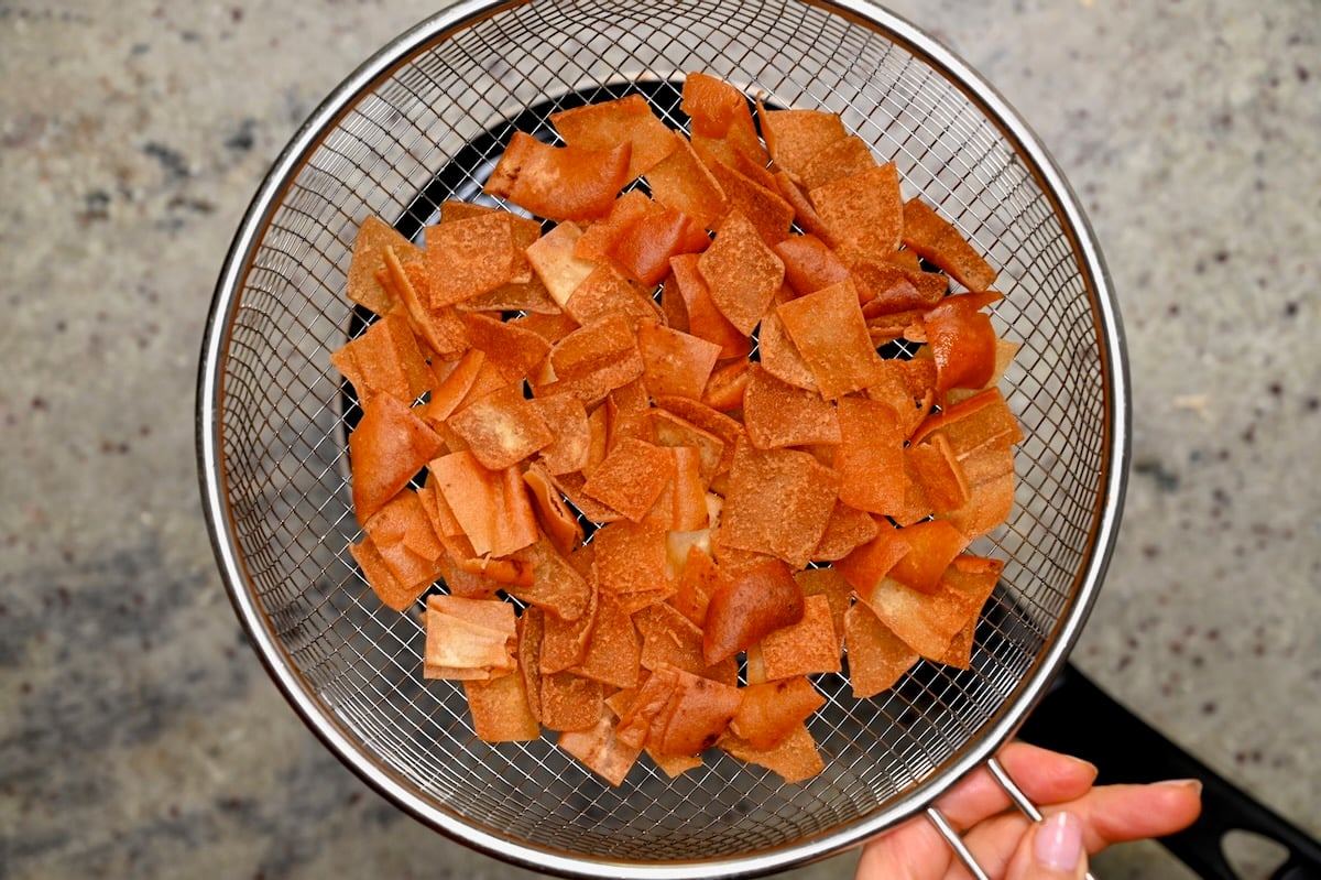 Crispy pita chips draining in a wire strainer after frying.
