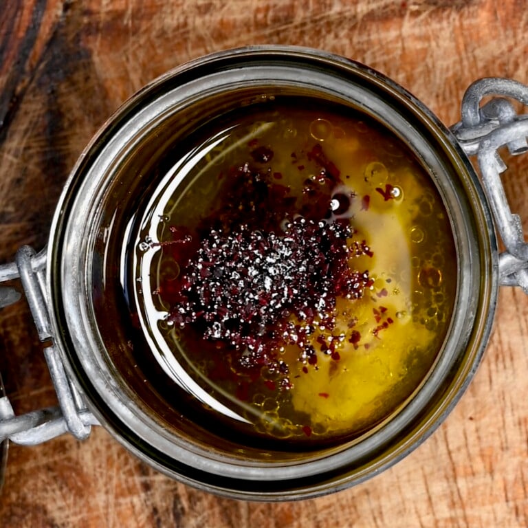 Top-down view of fattoush dressing in a small glass jar with olive oil and sumac.