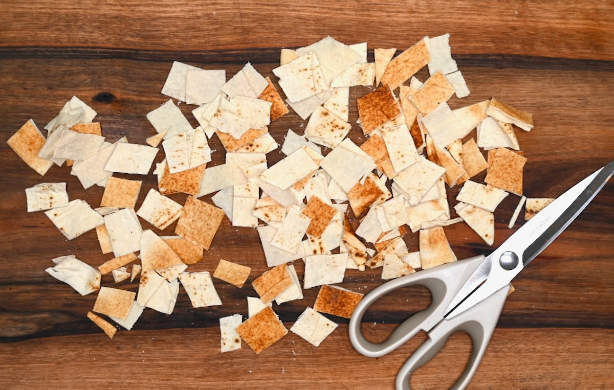 Cut pita squares on a cutting board with kitchen scissors for homemade pita chips.