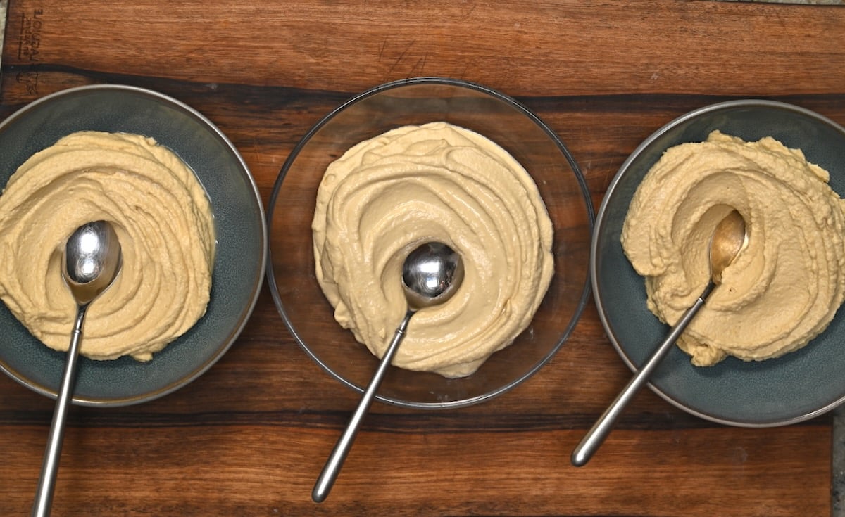 Three bowls of hummus with spoons, showing three texture variations made from canned chickpeas.