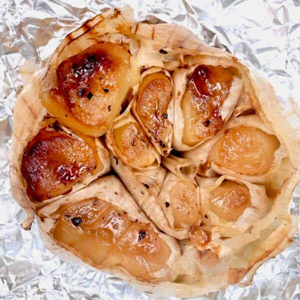 Close-up of a roasted garlic head on foil with soft, golden cloves and caramelized edges.