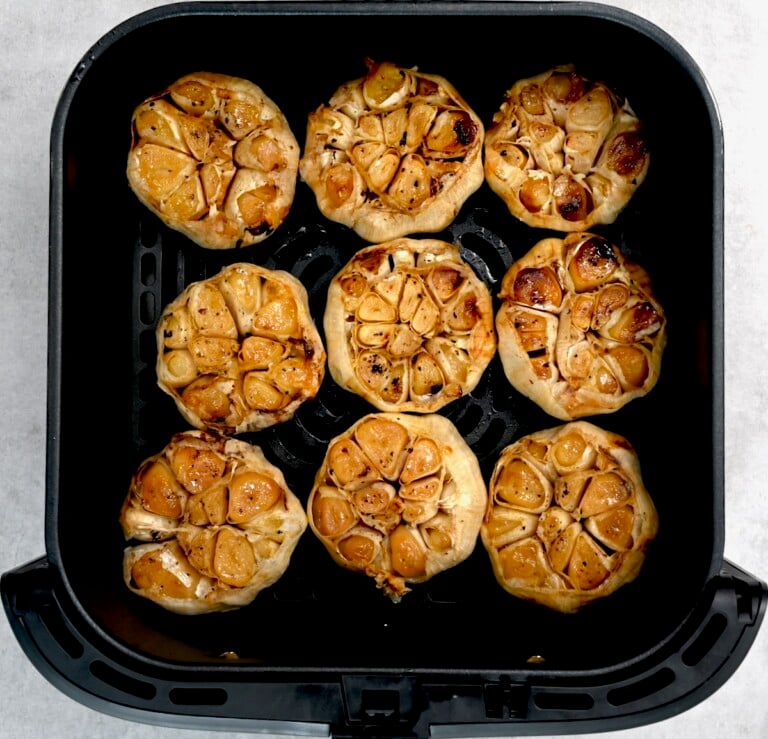 Roasted garlic heads in an air fryer basket, cooked until soft and golden.