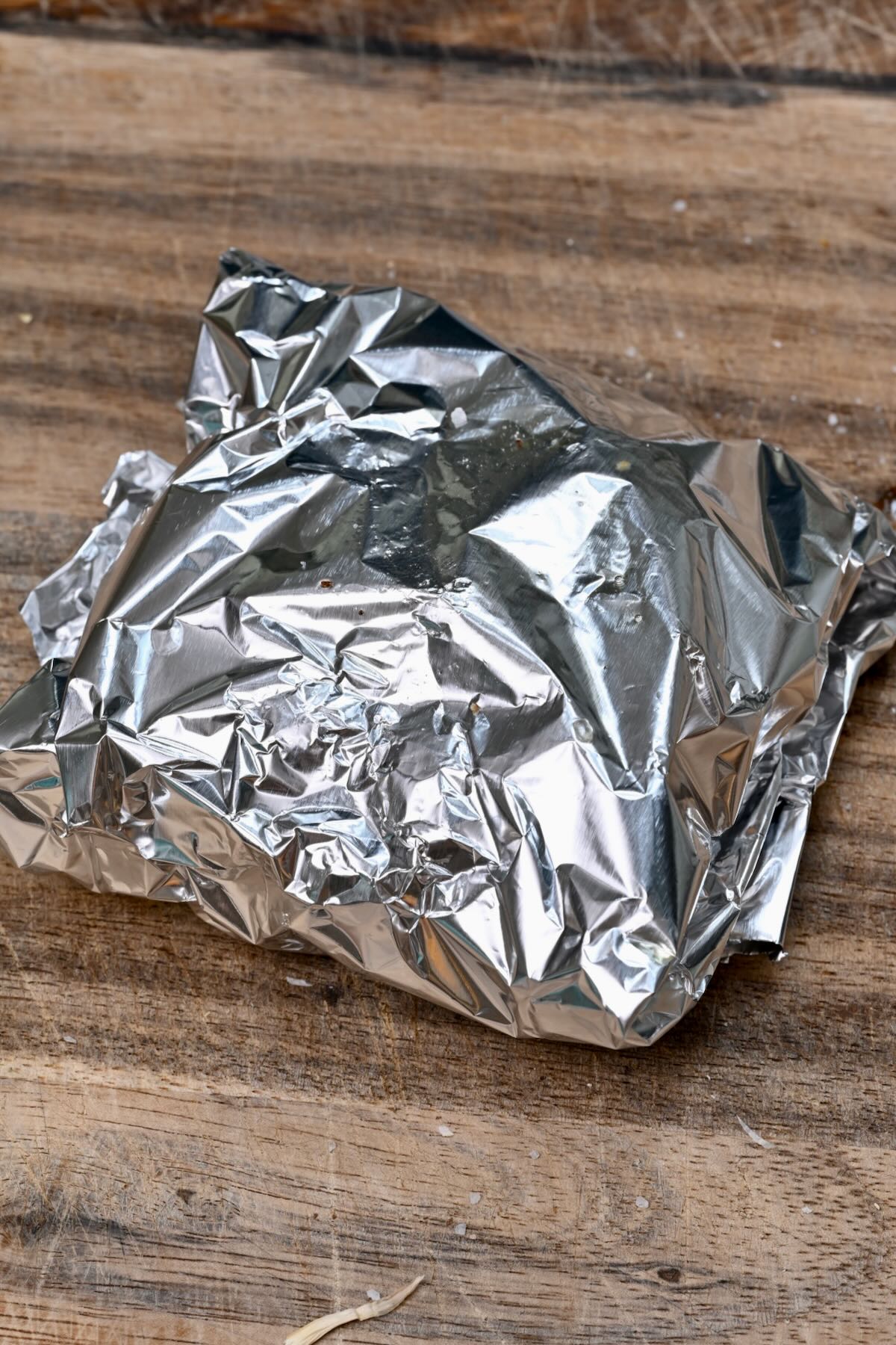 Foil-wrapped garlic packet on a wooden cutting board, ready for roasting.
