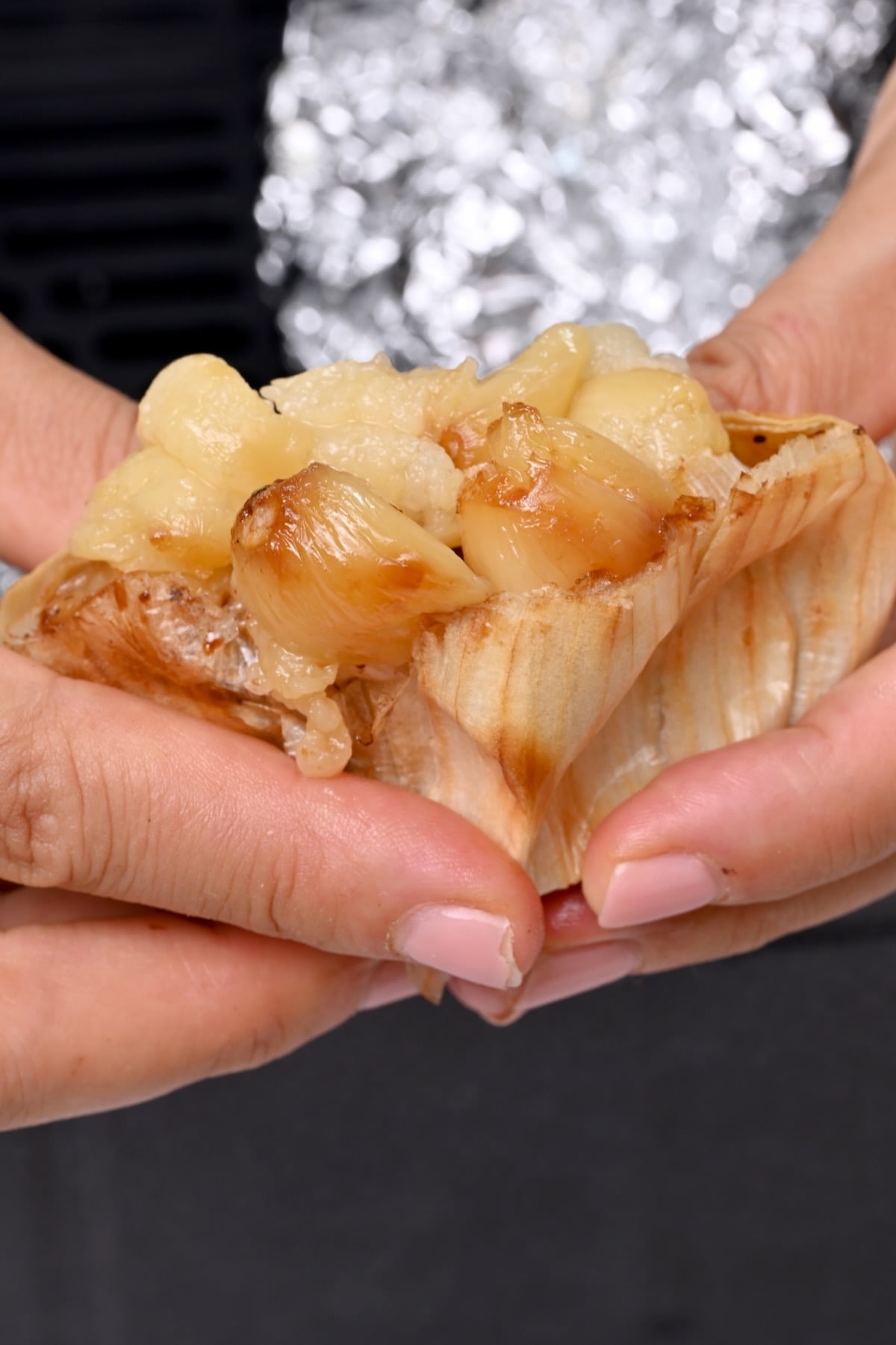 Close-up of soft roasted garlic cloves being squeezed from a garlic head by hand.