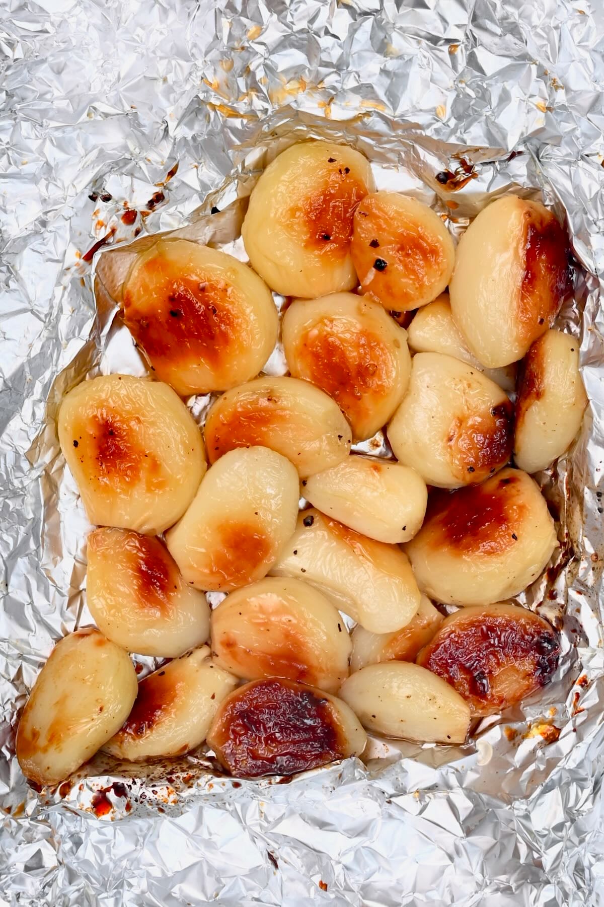 Roasted garlic cloves on foil, soft and golden with lightly caramelized tops.
