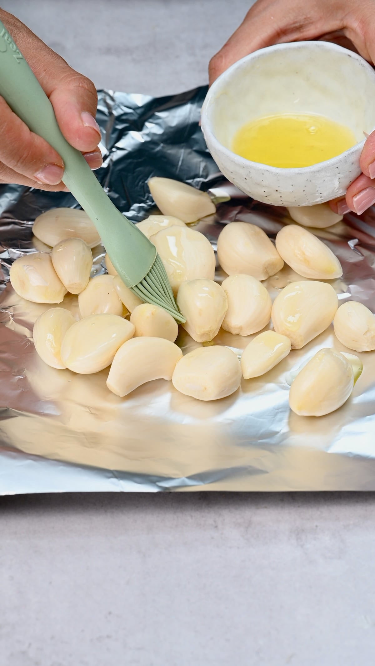 Peeled garlic cloves brushed with olive oil on a sheet of foil before roasting.