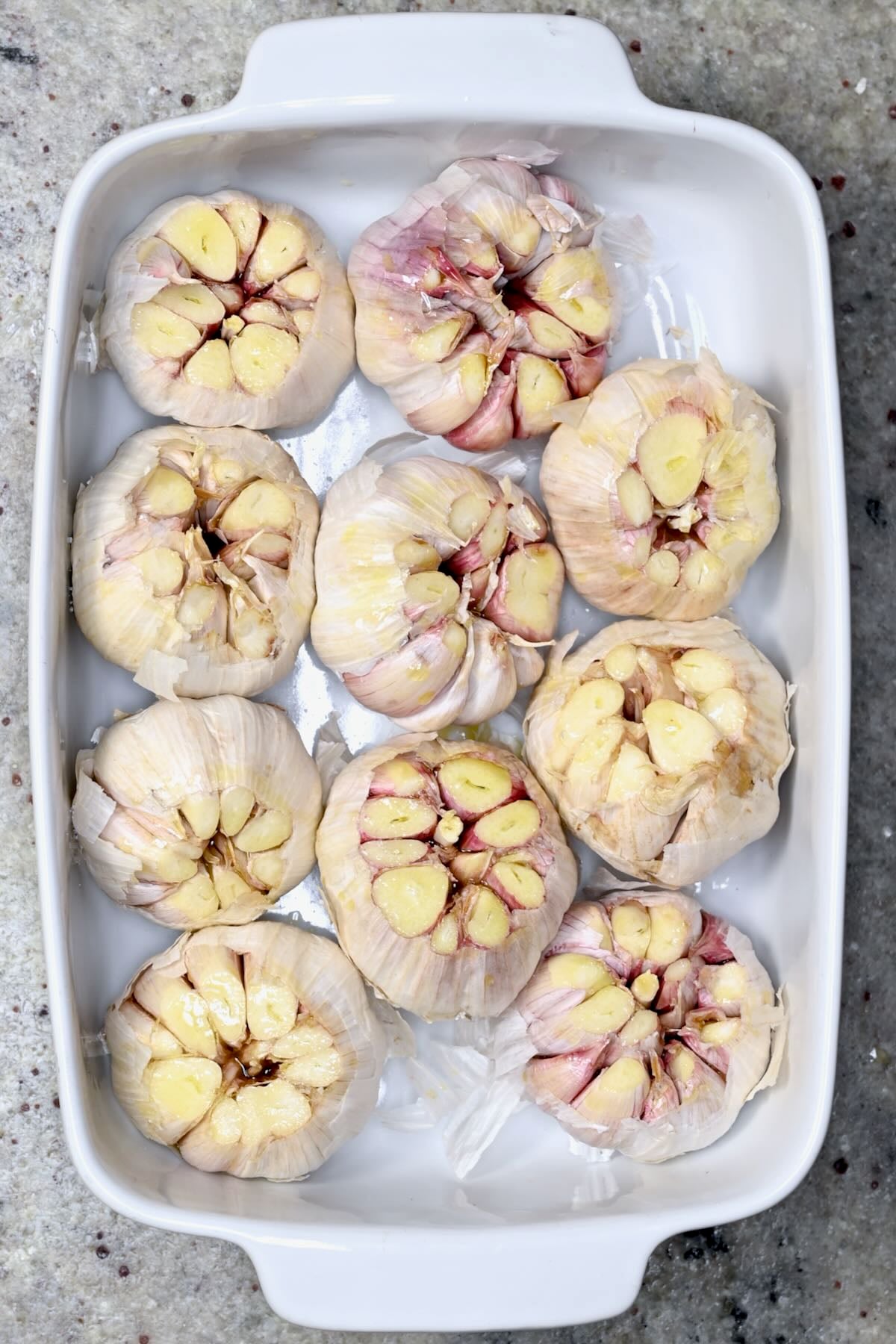 Cut garlic heads arranged in a baking dish before roasting.