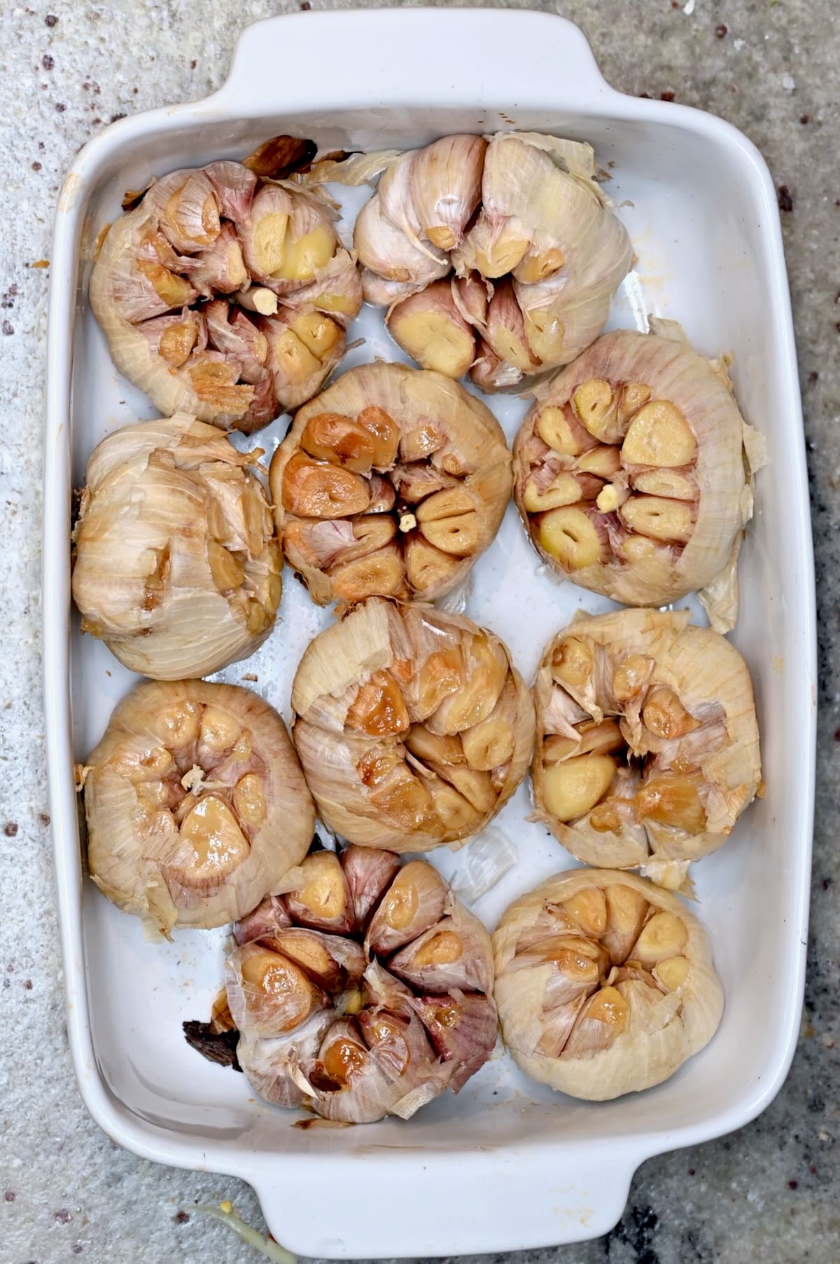 Roasted garlic heads in a baking dish after cooking, with soft golden cloves.
