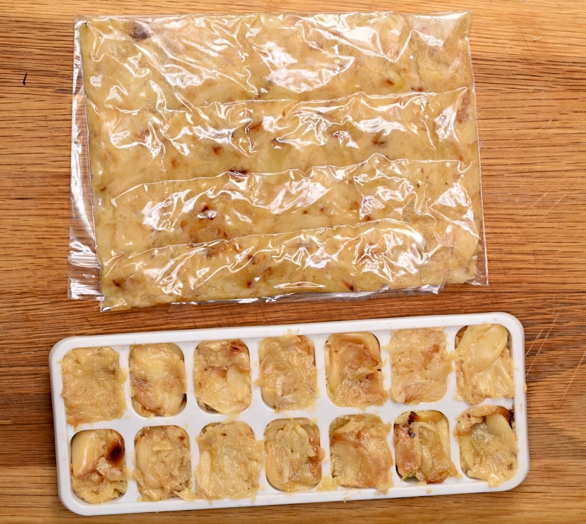 Roasted garlic stored in a freezer bag and portioned into an ice cube tray on a wooden surface.