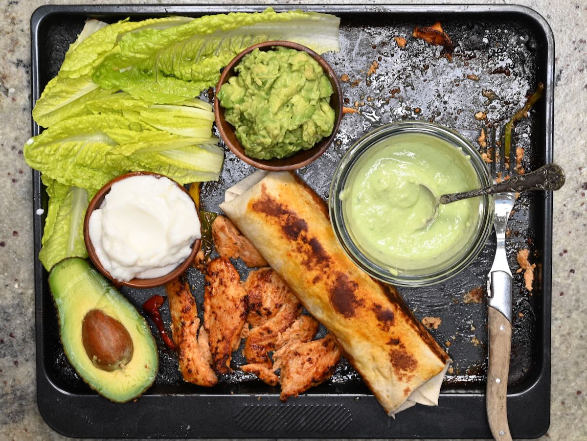 Baked chicken tenders with sauce, guacamole, and lettuce leaves next to them.