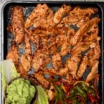 Baked chicken tenders on a tray with lettuce leaves, fajita peppers, and guacamole.