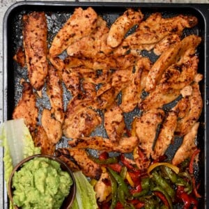 Baked chicken tenders on a tray with lettuce leaves, fajita peppers, and guacamole.