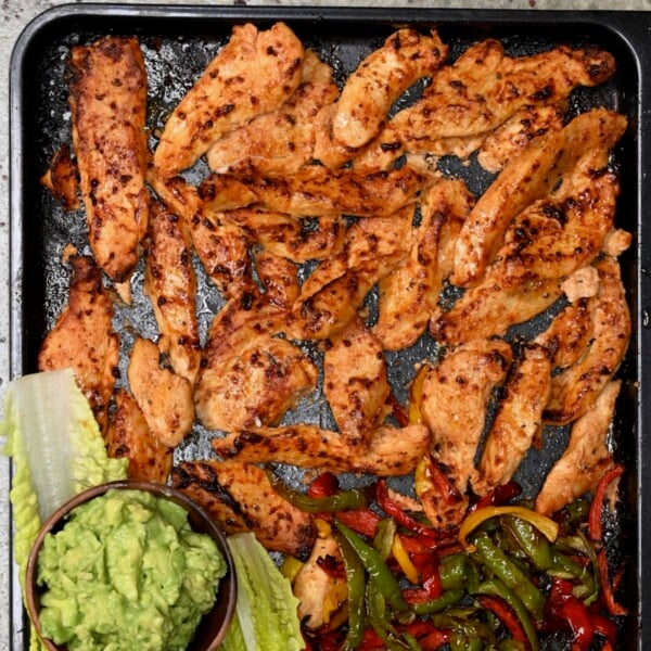 Baked chicken tenders on a tray with lettuce leaves, fajita peppers, and guacamole.