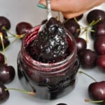 A spoonful of cherry jam over a small jar.