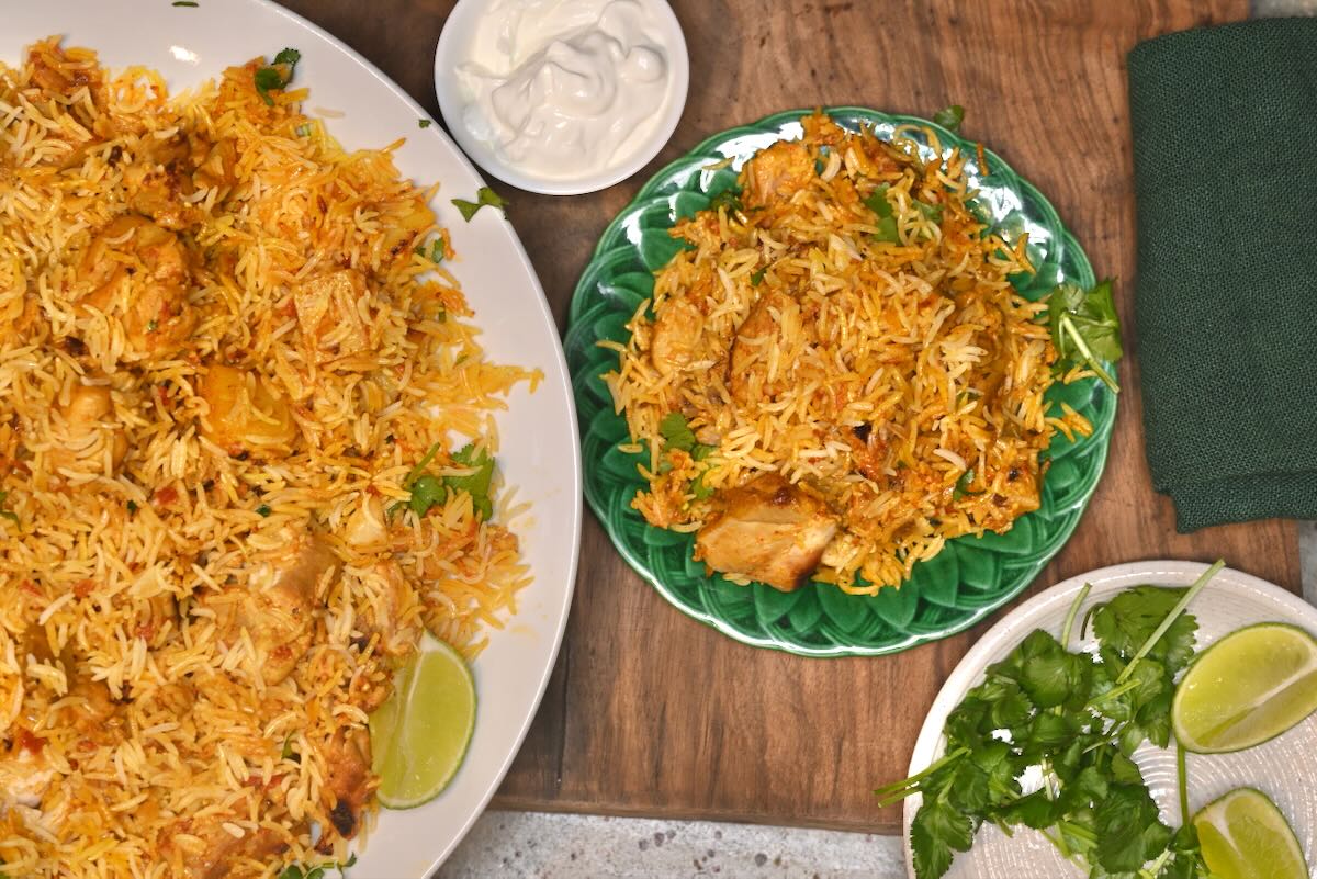 A serving of chicken biryani on a green plate next to the whole dish.