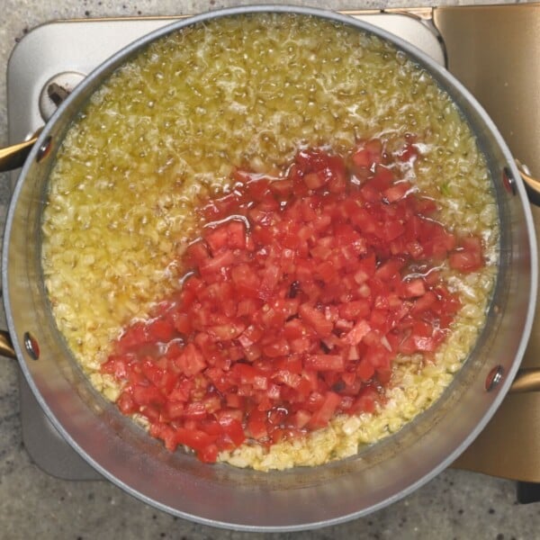 Adding chopped tomatoes to the saucepan.