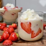 A dessert glass with fresas con crema topped with whipped cream. and strawberries next to it.