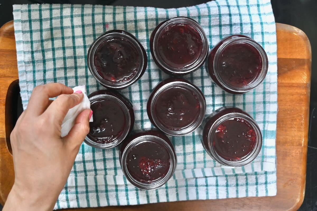 Cleaning the rims of jars filled with homemade jam.