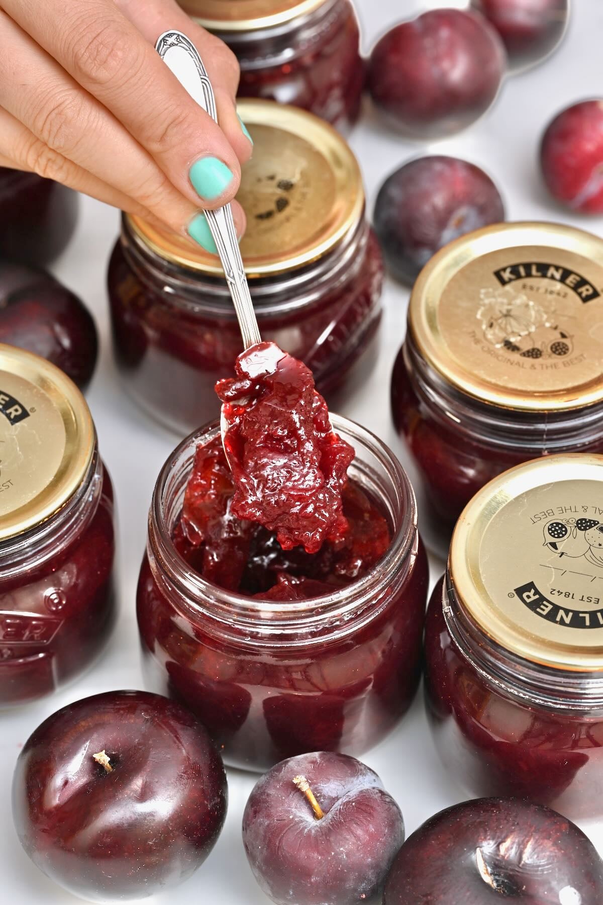 A spoonful of homemade plum jam above its jar.