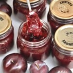 A spoonful of homemade plum jam above its jar.
