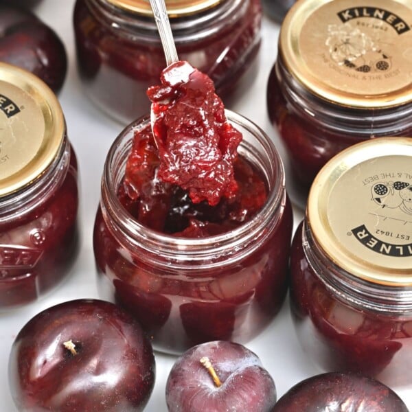 A spoonful of homemade plum jam above its jar.