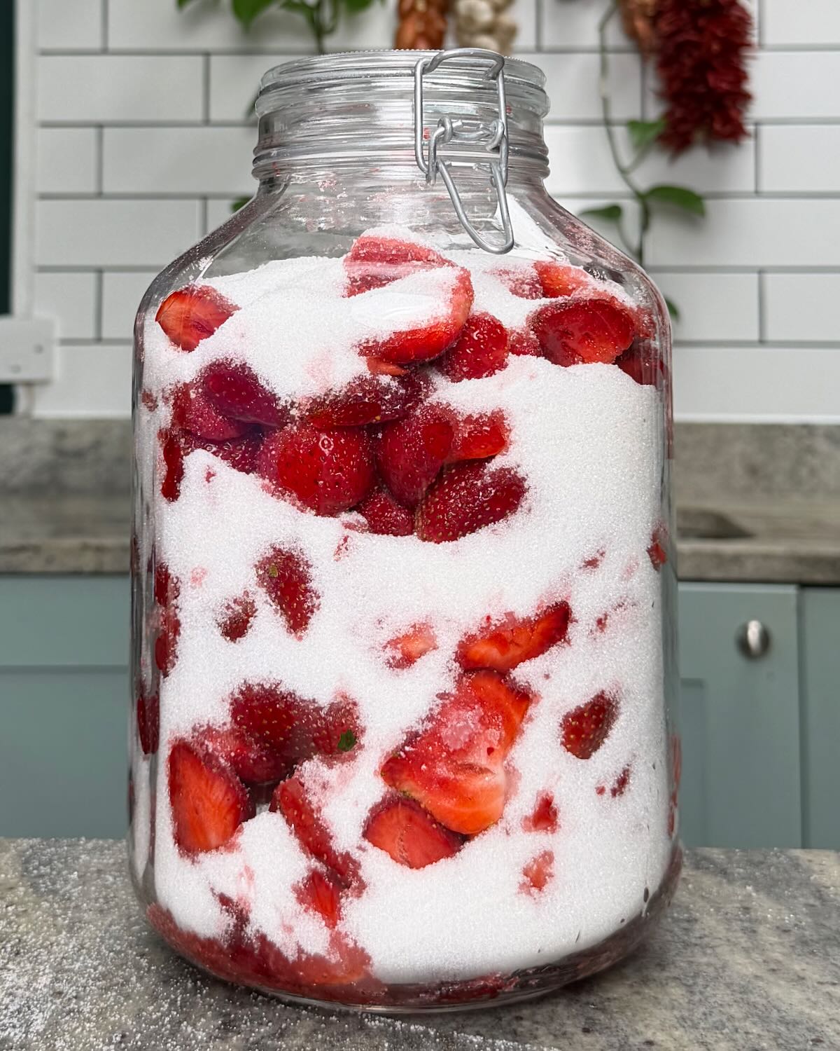 A large jar filled with strawberries and sugar.