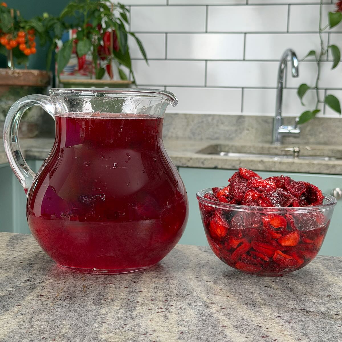 Strawberry cheong syrup filtered out in a pitcher with the strawberry pieces in a bowl.