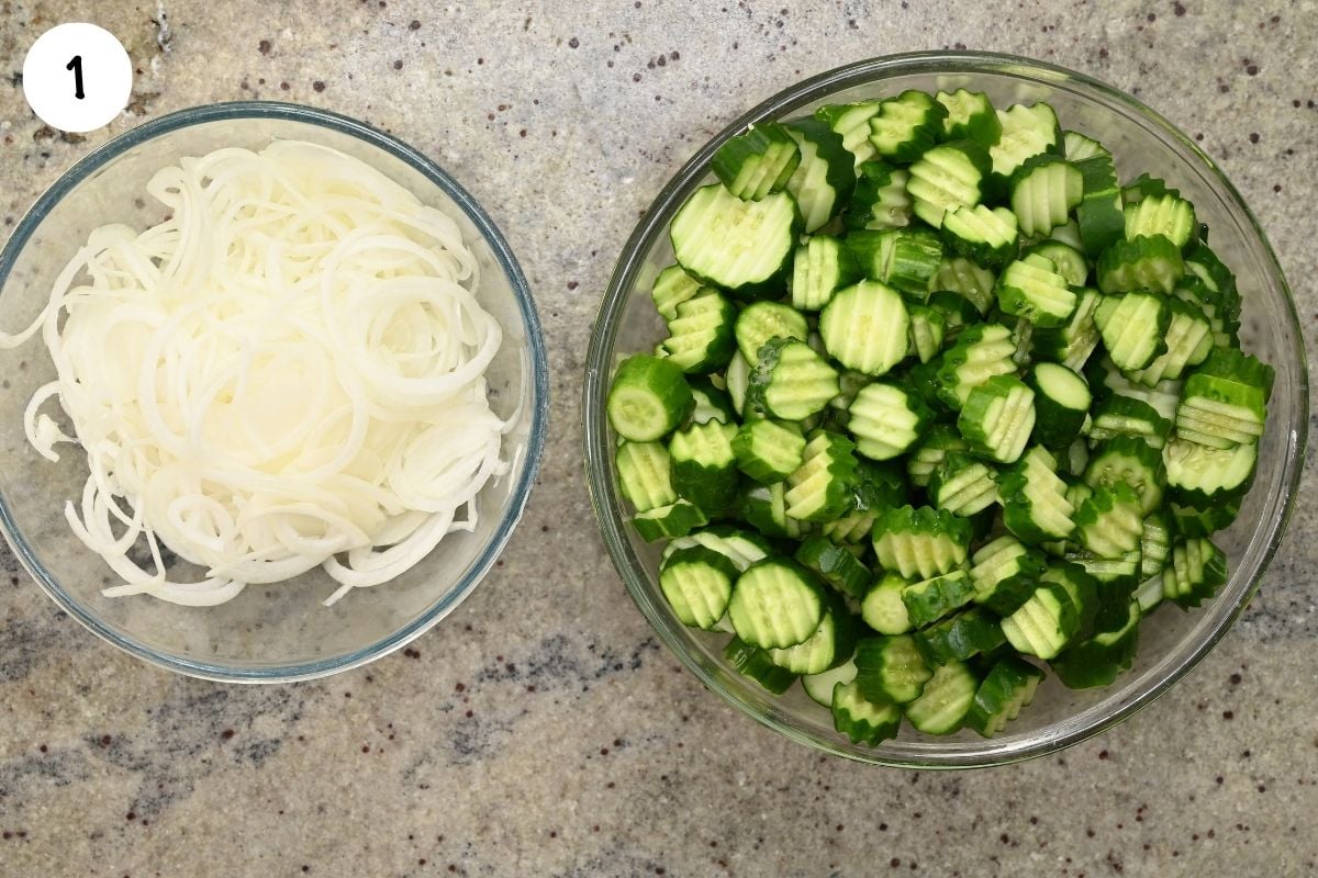 Top-down view of two glass prep bowls containing crinkle-cut cucumber slices and thinly sliced white onion.