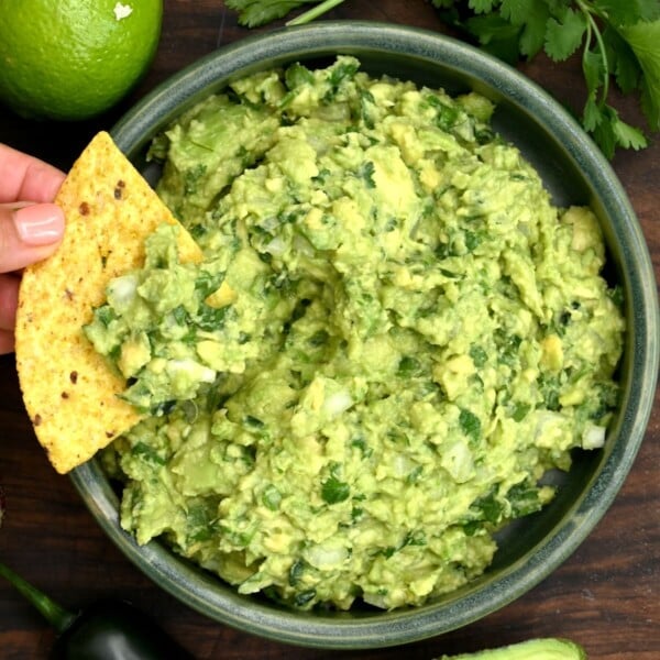 Guacamole in a small bowl with a tortilla chip dipping into it.