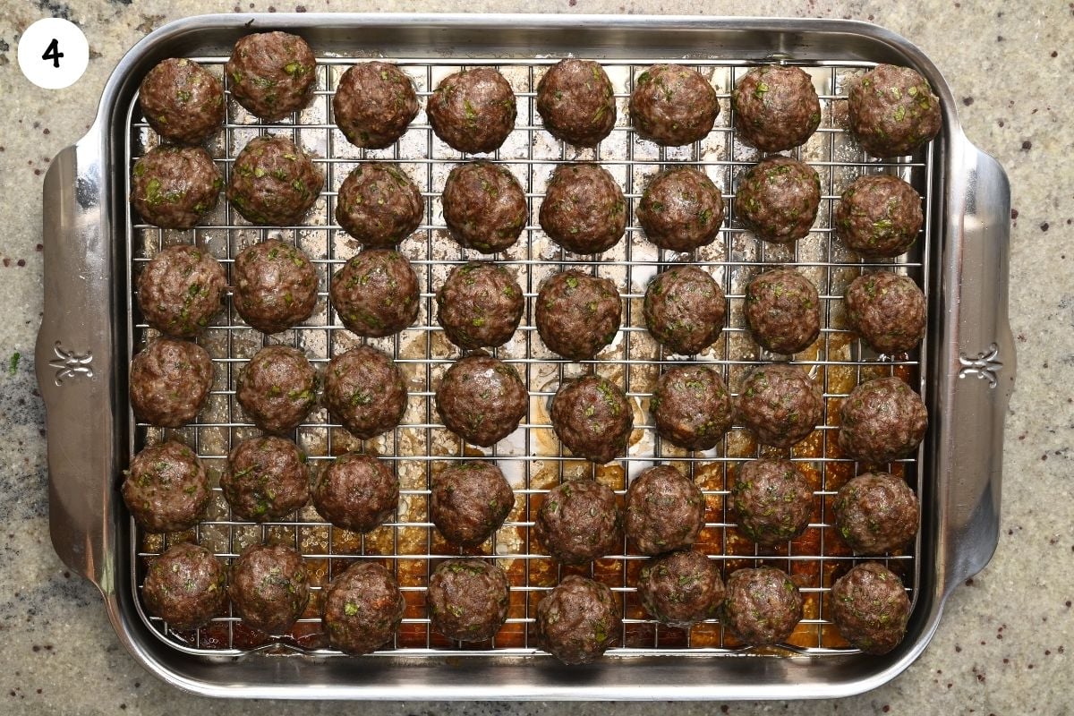 Top-down view of browned, fully cooked kofta meatballs arranged in neat rows on a wire rack over a stainless steel baking tray.