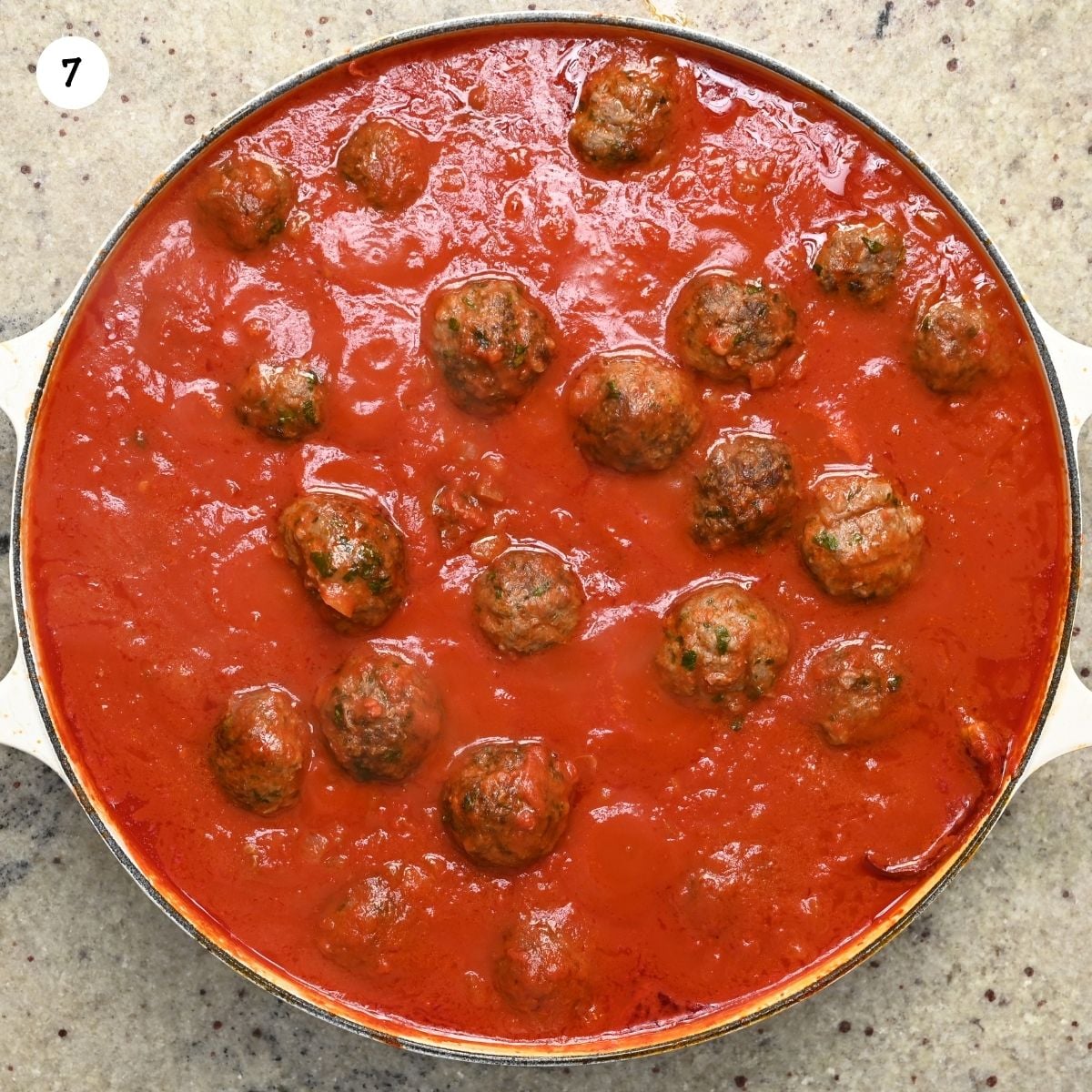 Top-down view of kofta meatballs simmering in a wide skillet filled with thick, vibrant red tomato sauce.