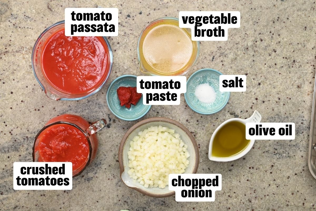 Top-down view of ingredients for kofta meatball tomato sauce, including tomato passata, crushed tomatoes, vegetable broth, tomato paste, chopped onion, olive oil, and salt arranged on a countertop.