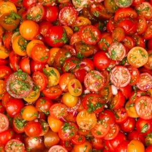 Close-up view of vibrant red, orange, and yellow cherry tomato halves tossed with chopped herbs and minced red onion.