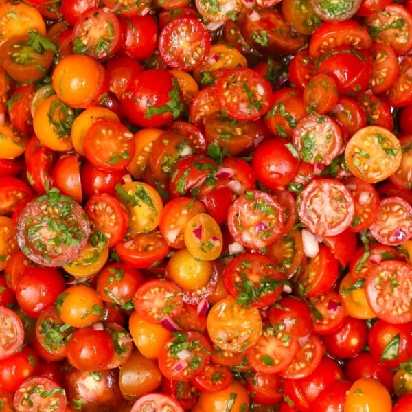 Close-up view of vibrant red, orange, and yellow cherry tomato halves tossed with chopped herbs and minced red onion.