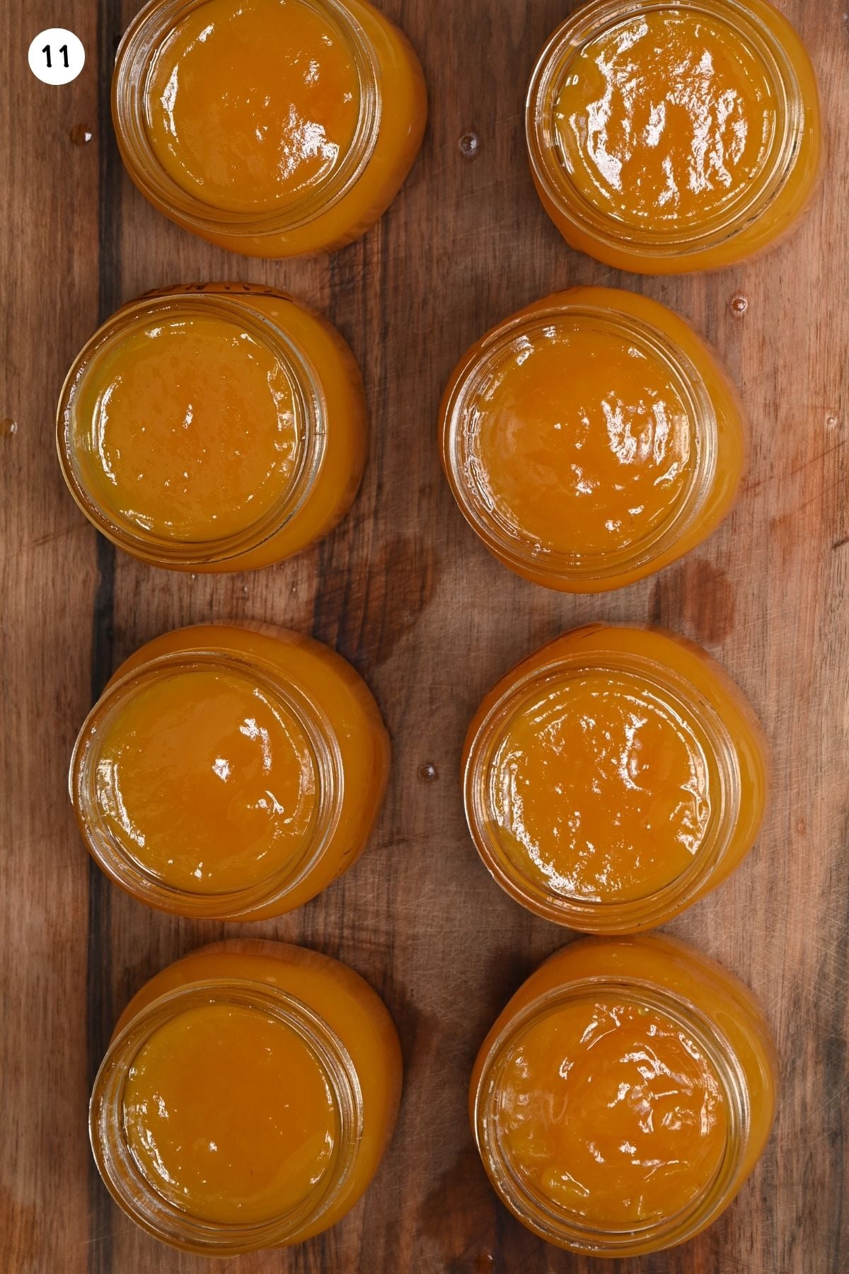 Top-down view of eight open glass canning jars filled with golden, smooth peach butter arranged in two rows on a rustic wooden board.