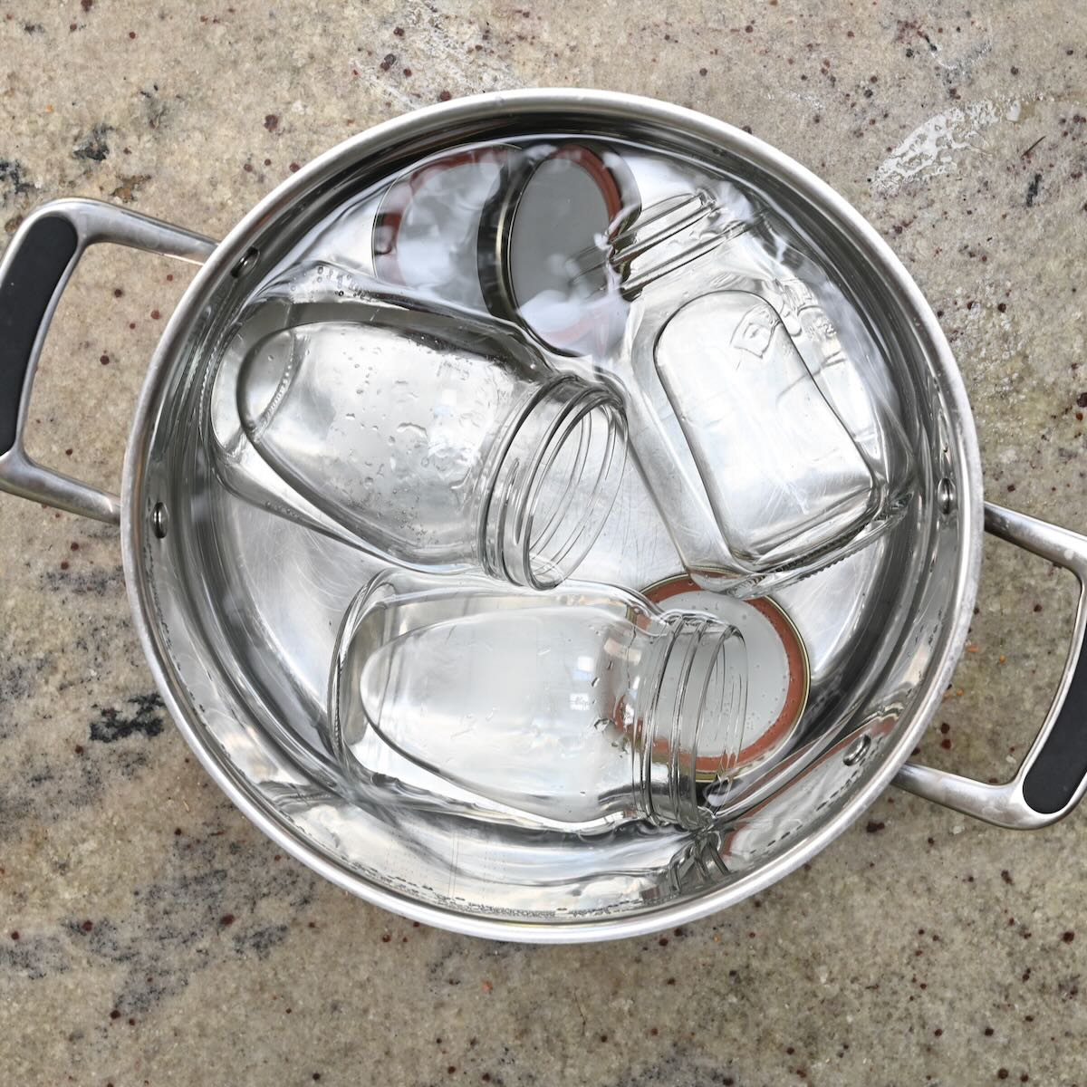 Glass mason jars and metal lids submerged in a large pot of boiling water.