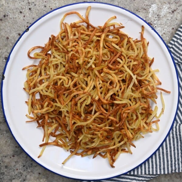 Top-down view of a pile of crispy, thin golden-brown shoestring fries served on a white enamel plate with a blue rim.