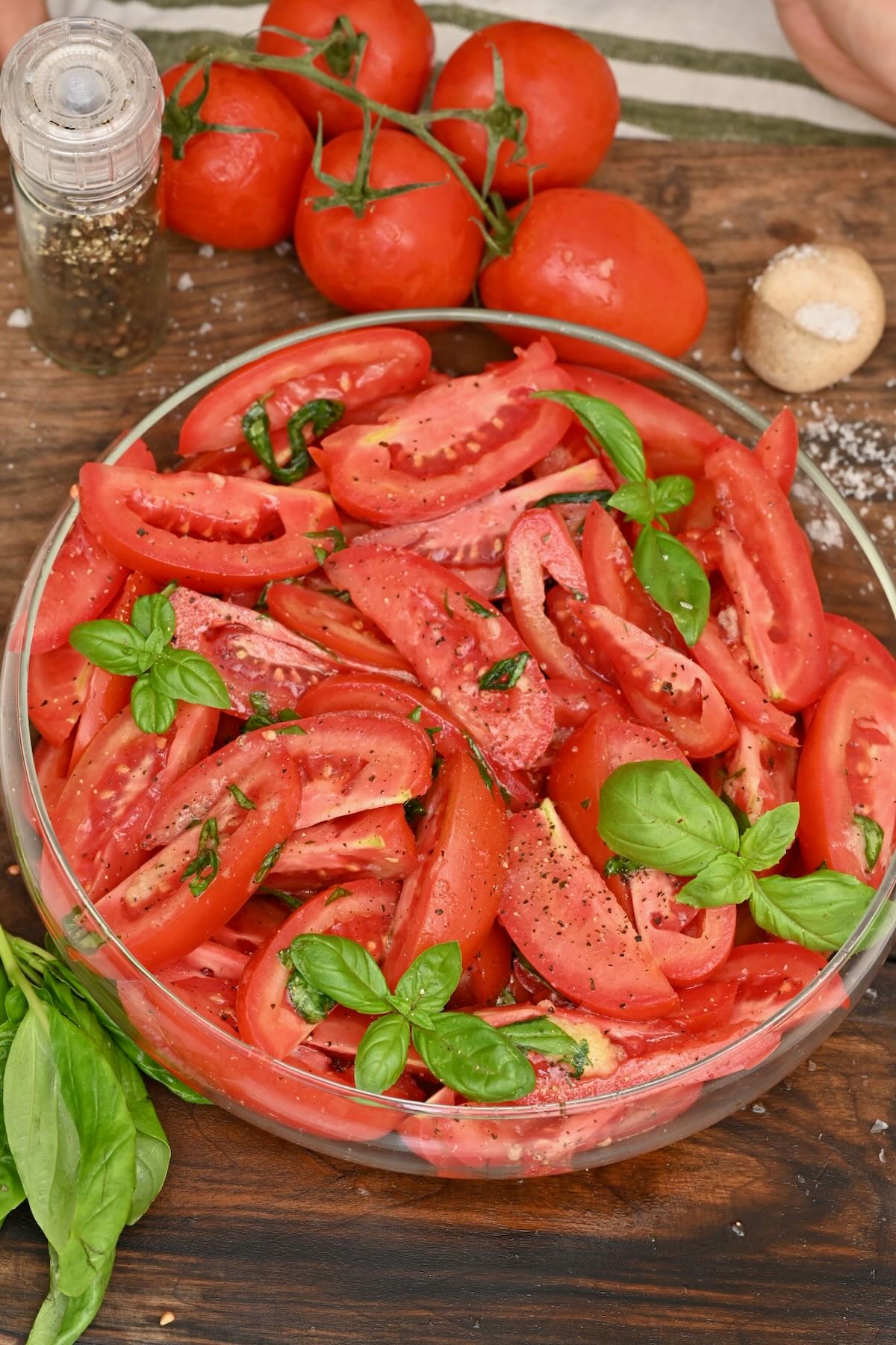 Vertical view of a simple tomato salad in a round glass dish set against a rustic wooden backdrop.