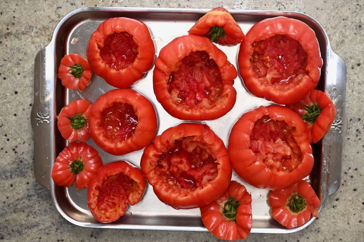 Empty, hollowed tomato shells lined up on a stainless steel baking sheet ready to be filled.