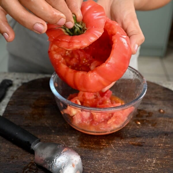 Hands scooping out the inside pulp of a fresh beefsteak tomato.