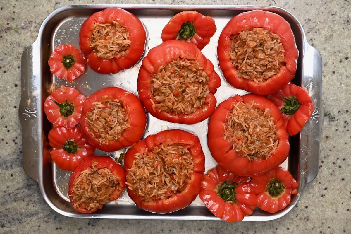 Red tomato shells filled with savory rice and ground meat stuffing on a metal tray.