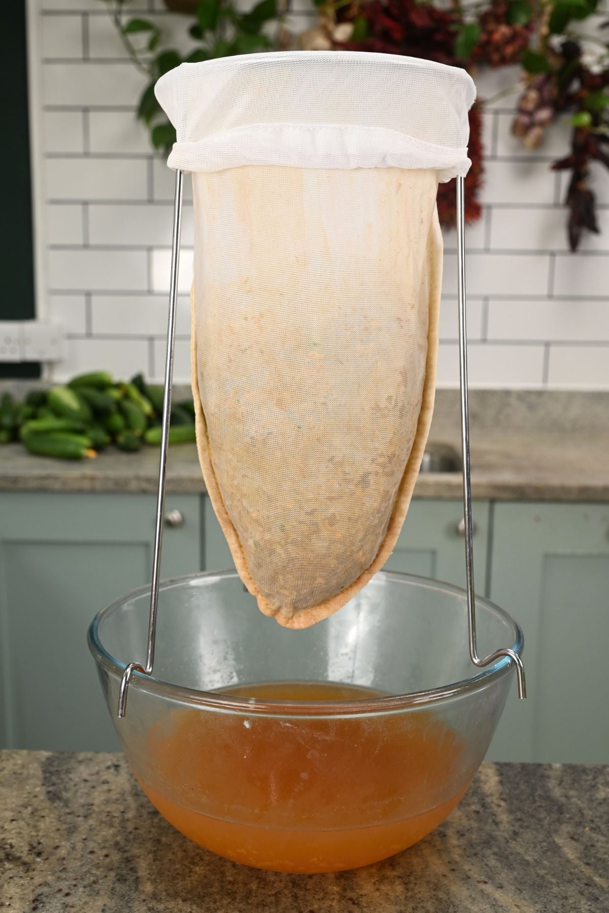 A mesh jelly bag hanging over a large glass bowl as freshly strained golden-amber verjuice collects at the bottom.