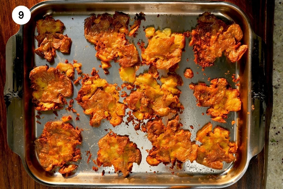 A top-down view of smashed red potatoes roasted to a golden, crispy perfection on a metal baking tray.