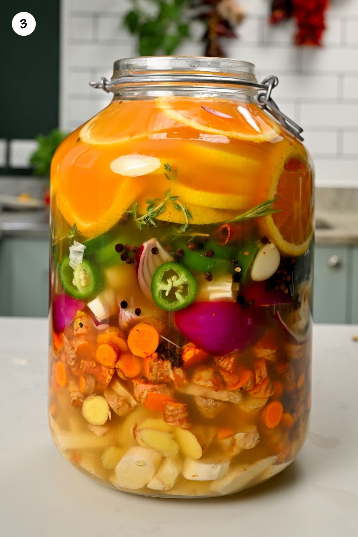 A large glass jar filled with layered fire cider ingredients submerged in liquid apple cider vinegar.