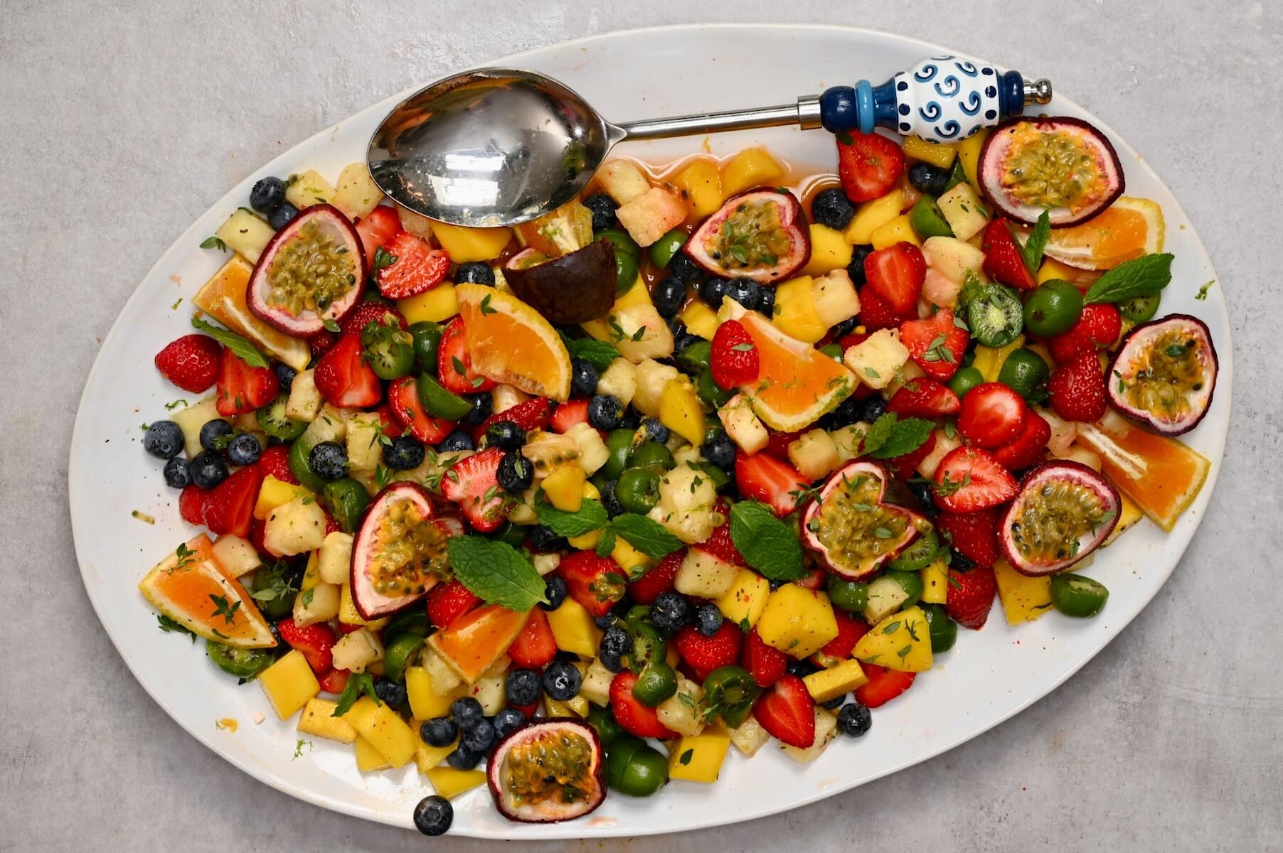 A large serving dish with freshly made fruit salad topped with passion fruit and orange slices.