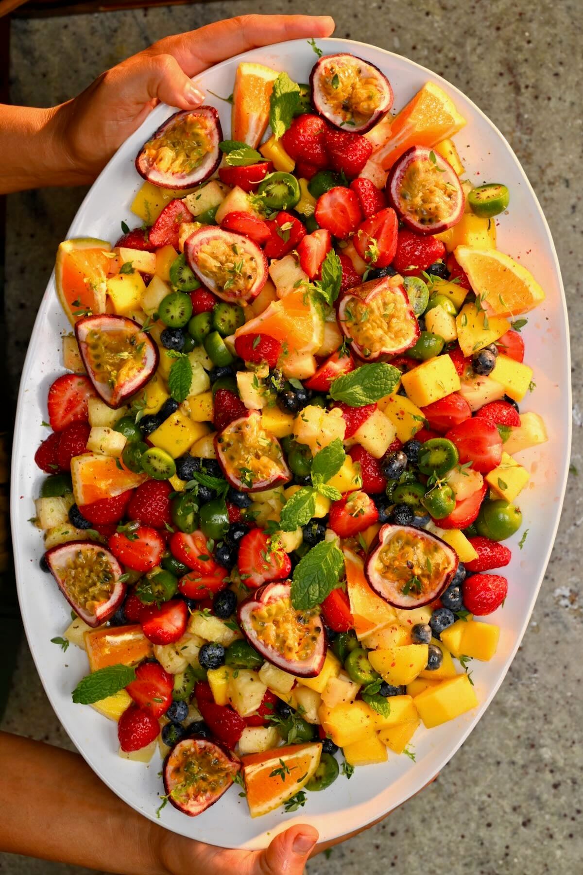 A large serving dish with freshly made fruit salad topped with passion fruit and orange slices.