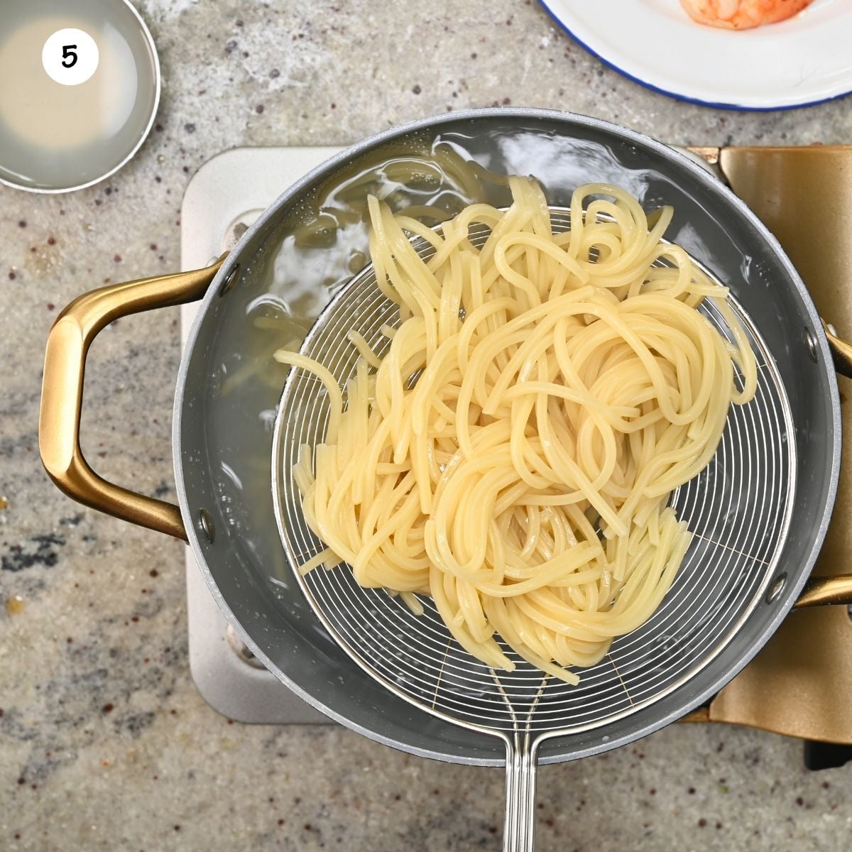 Cooked spaghetti noodles being lifted out of a pot of boiling water with a mesh spider skimmer.