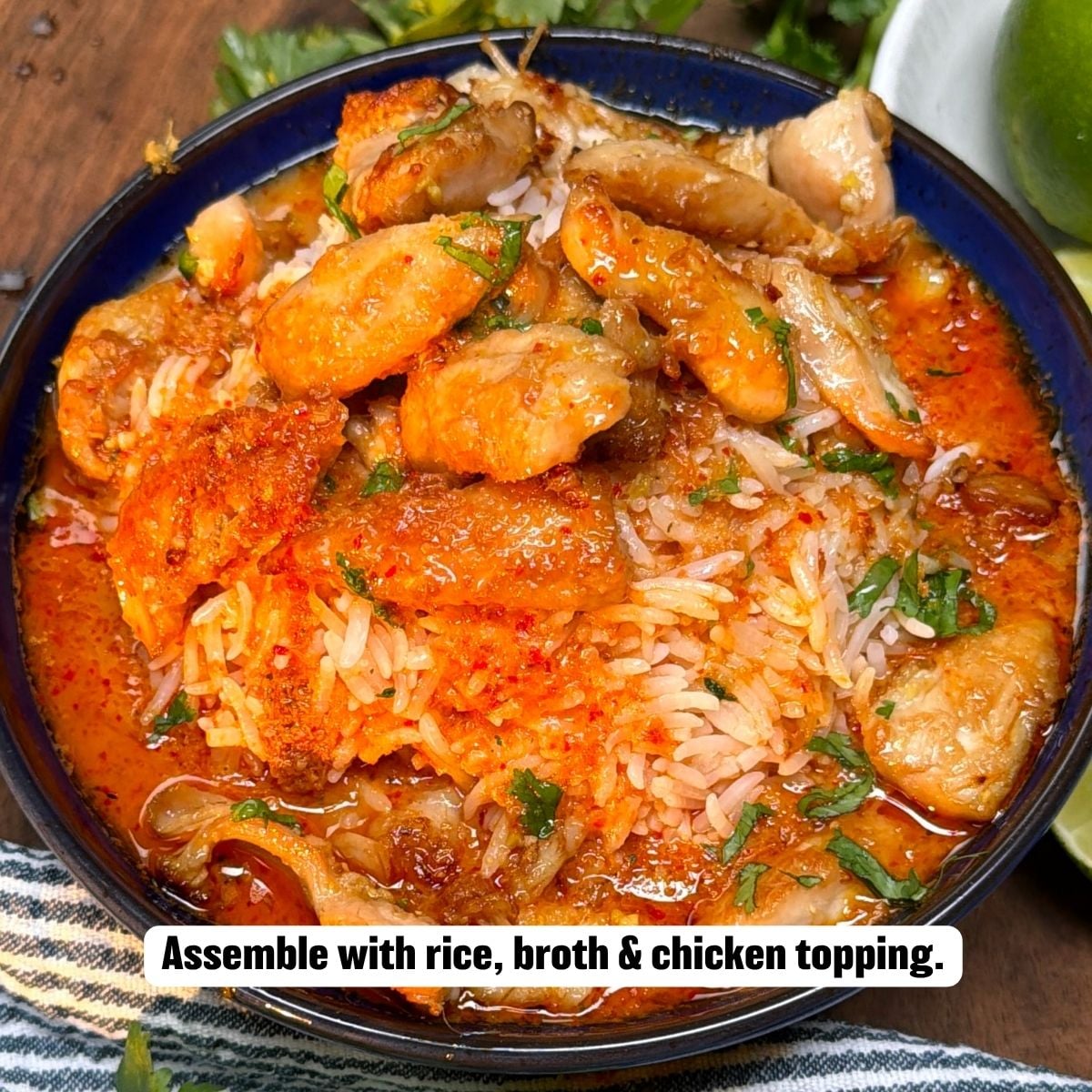 A top-down view of a dark blue serving bowl filled with jasmine rice and rich red curry broth, topped with tender seared chicken pieces and garnished with fresh cilantro, with lime wedges on the side.