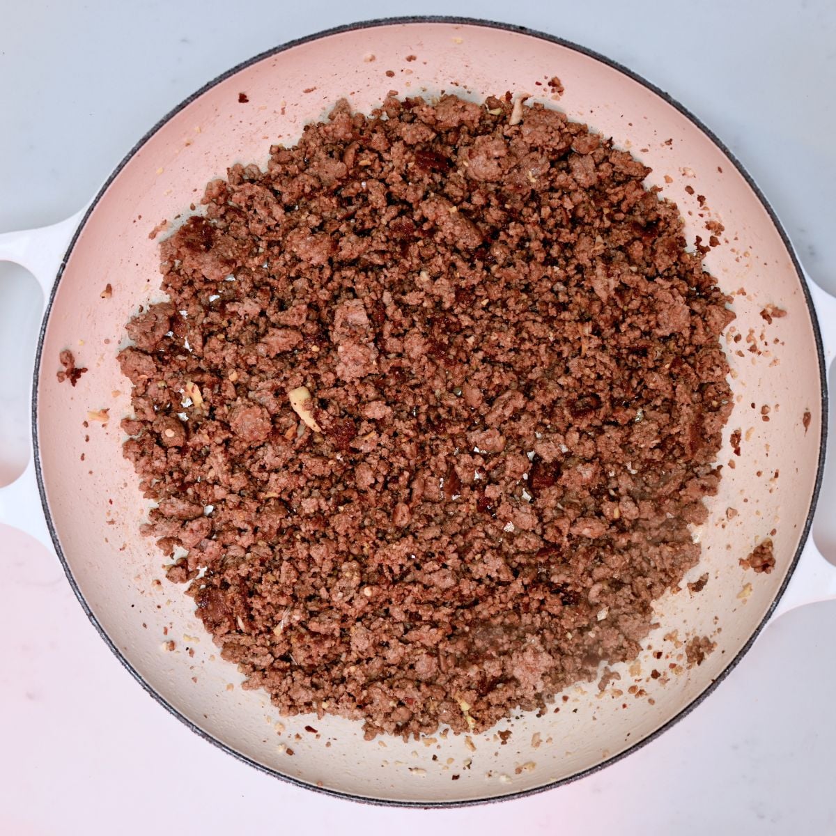 A top-down view of seasoned ground beef browned and crumbled evenly across a large enamel skillet.